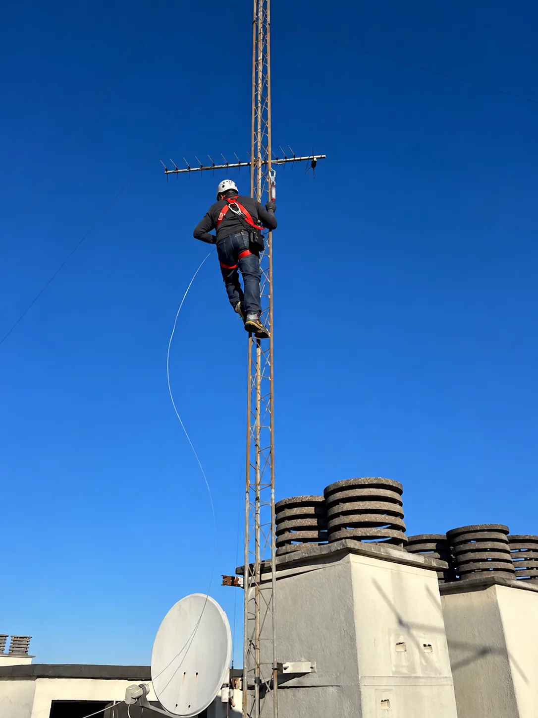 Antenniste TELEANTEN grimpant sur un mât d'antenne râteau TNT, parabole en contrebas