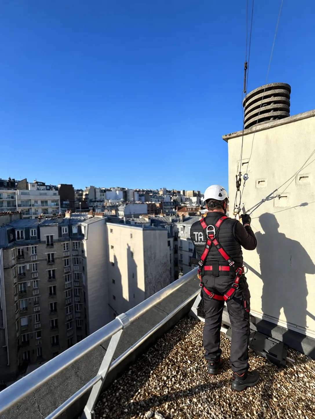 Antenniste TELEANTEN sécurisé par un câble de vie près d'une souche de cheminée sur un toit-terrasse